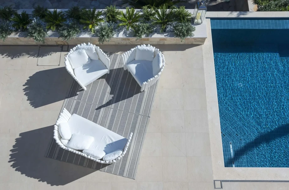 A stylish white lounge chair is beside a swimming pool, offering a serene spot for relaxation in pet-friendly Villa Acoona.