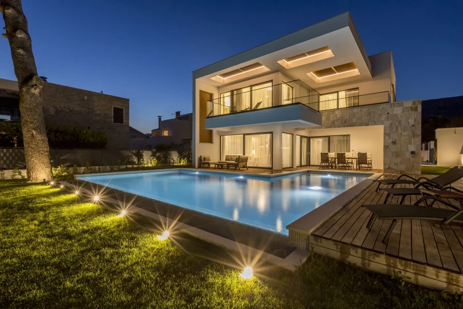 Modern luxury villa in Kaštela near Split at night, featuring a large illuminated private pool, contemporary architecture, and a spacious terrace with sun loungers.