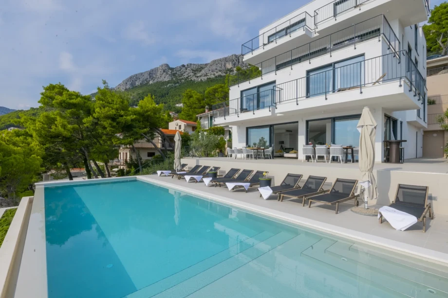 A spacious swimming pool with sun loungers is located in front of the luxurious Villa Bello