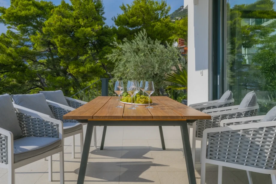 A table with grapes and glasses on it, surrounded by six chairs