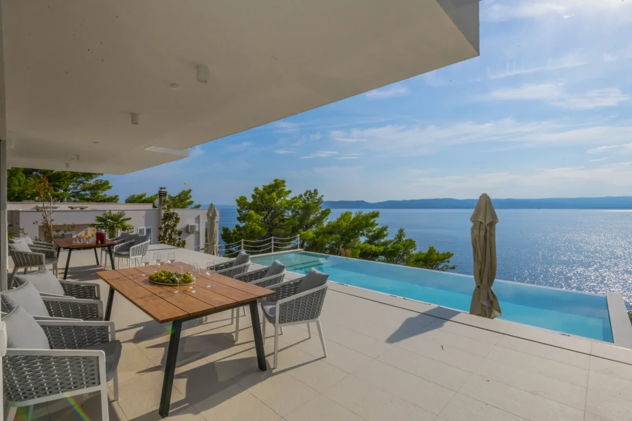 A table with chairs, a pool, and a view of the sea and an island