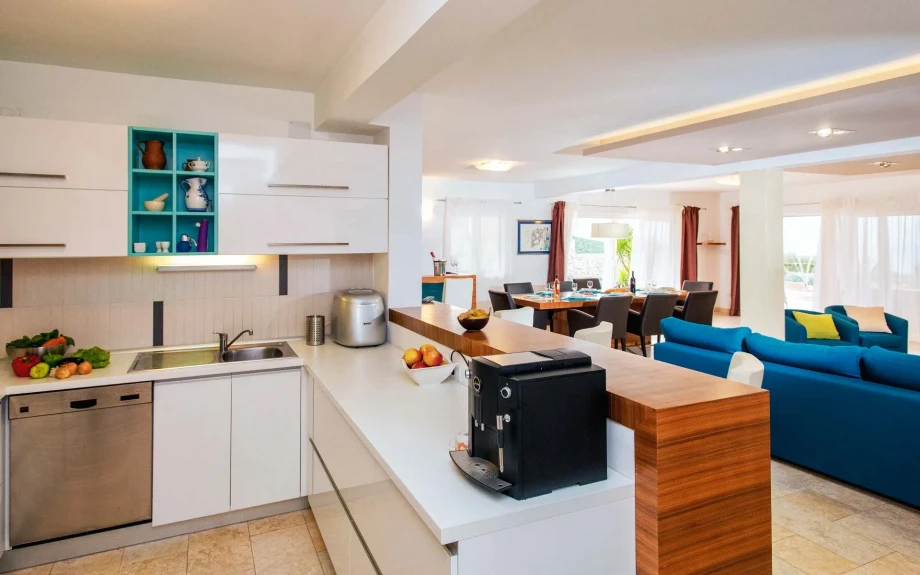 A spacious white kitchen with a coffee machine, fresh fruit and vegetables and a bar that separates it from the living room