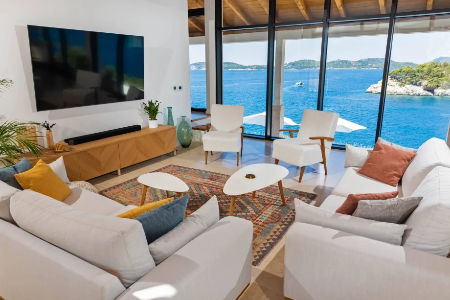 Gorgeous living room in the luxurious villa My Place, featuring a sofa, comfortable armchairs, a TV mounted on the wall, and a stunning open view of the sea.