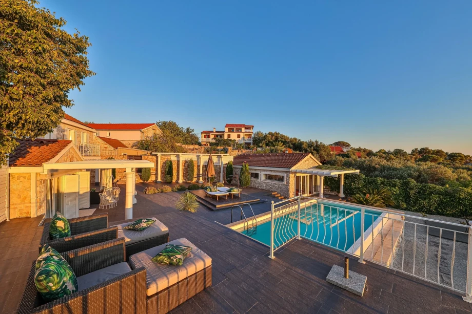 Modern design sun deck with loungers and parasols by the pool in front of modern Trogir villa complex for rent and vacation with a sea view.