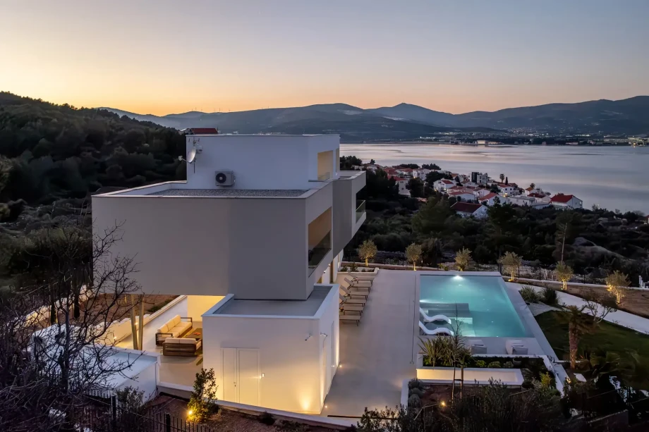 Sunset view of luxury villa Vista Maris featuring an illuminated pool and a stunning sea vista.