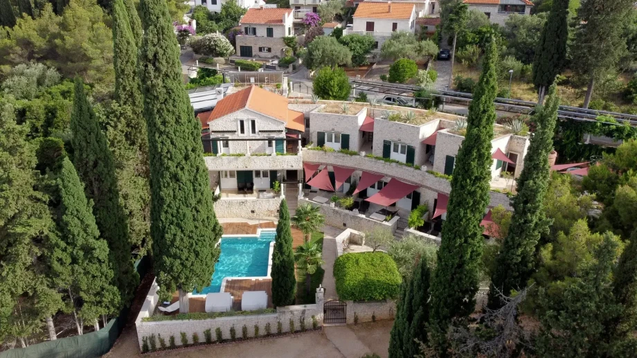 Aerial view of a luxury Villa Priska featuring a large swimming pool surrounded by lush greenery and outdoor seating areas.
