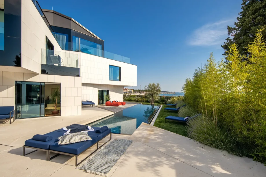 Bamboo fence with comfortable blue and red loungers around the pool, featuring a century-old olive tree at one end
