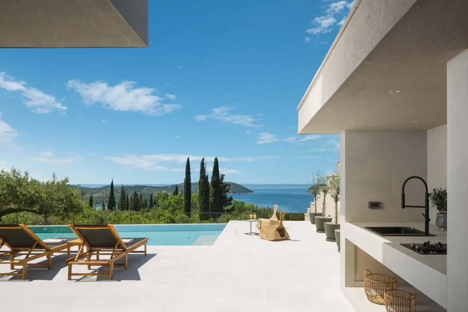 A swimming pool featuring sun loungers offers a stunning view of cypress trees and nearby islands