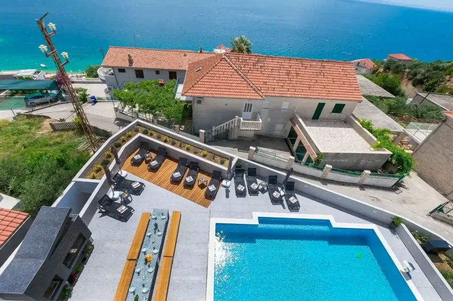 The exterior of the luxury family villa Grande Divina with outdoor heated pool, sun loungers, seating area, and sea view