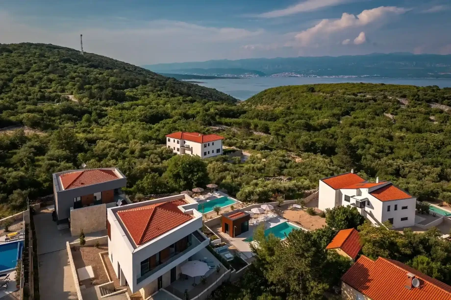 A villa nestled among lush trees with majestic mountains in the background, creating a serene natural setting.