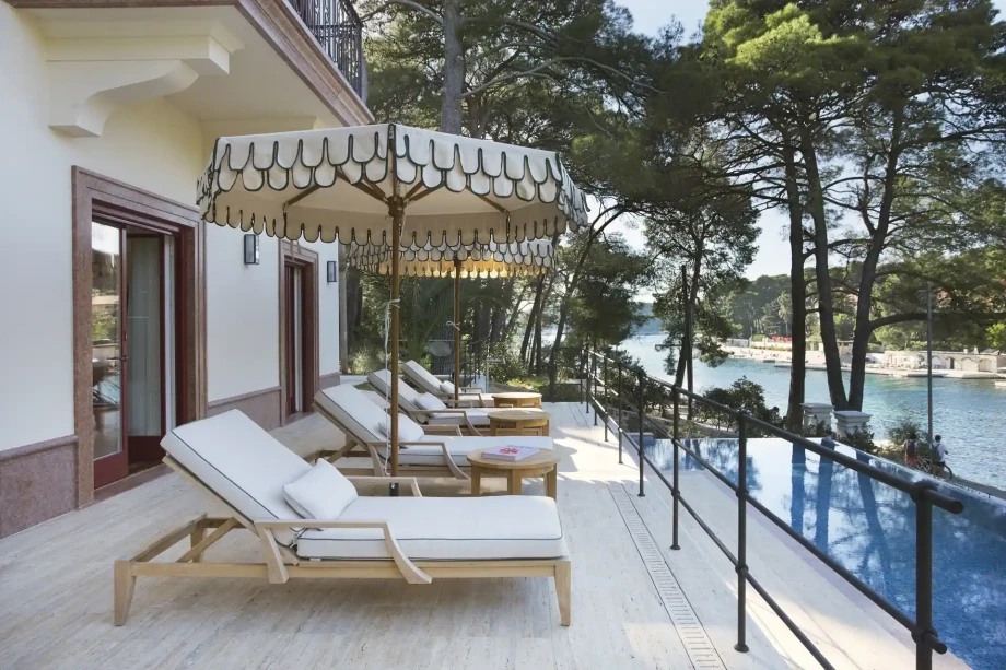 Porch by the pool with loungers and a parasol under century-old pines at luxury villa Nika.