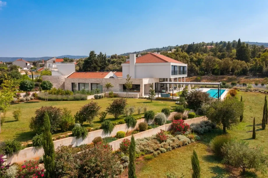 A spacious villa Hilltop Haven surrounded by a lush garden, with a swimming pool visible in the backyard.