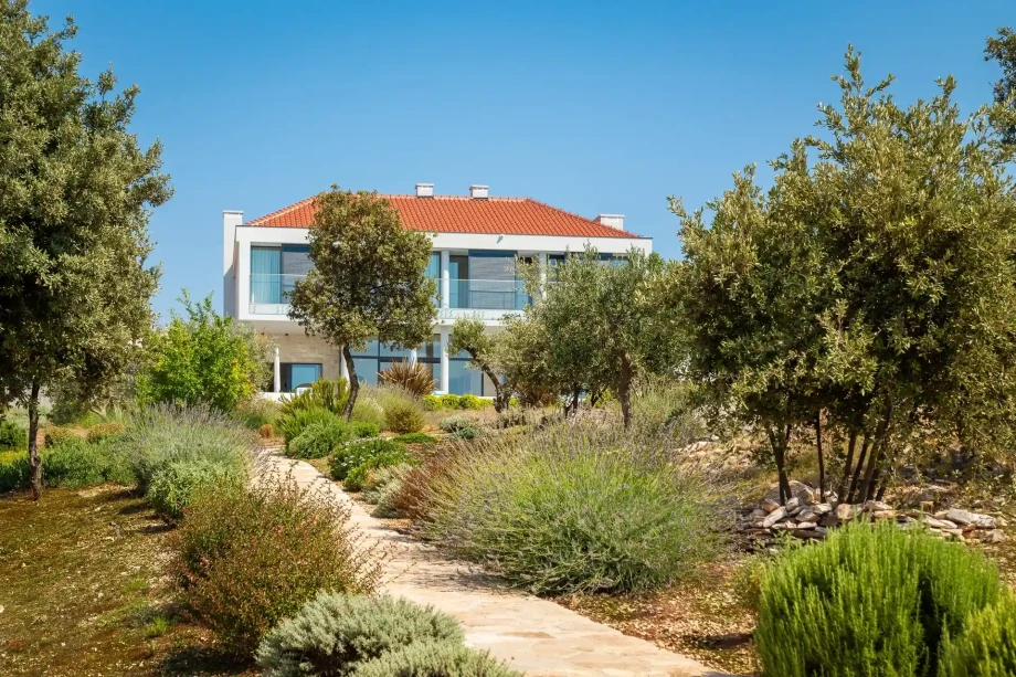 An elegant luxury villa situated on island Brac featuring a vibrant garden and trees in front, emphasizing its refined outdoor space.