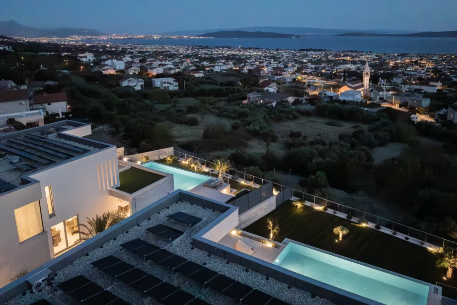 Aerial night photo of modern villa with a stunning pool and breathtaking sea views, perfect for a luxurious getaway.