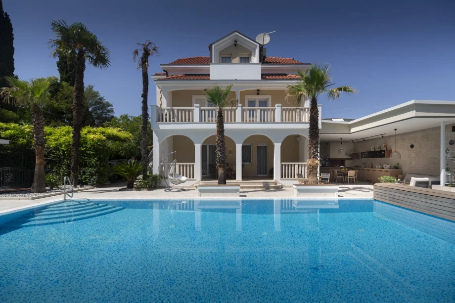 Luxury Villa Eterna with a swimming pool surrounded by greenery and a clear blue sky.